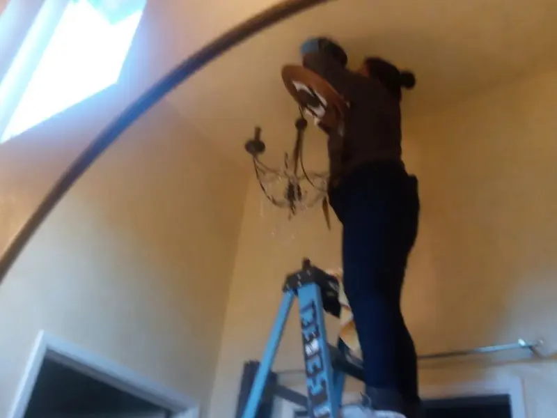 Electrician installing a chandelier in a Raynham residence